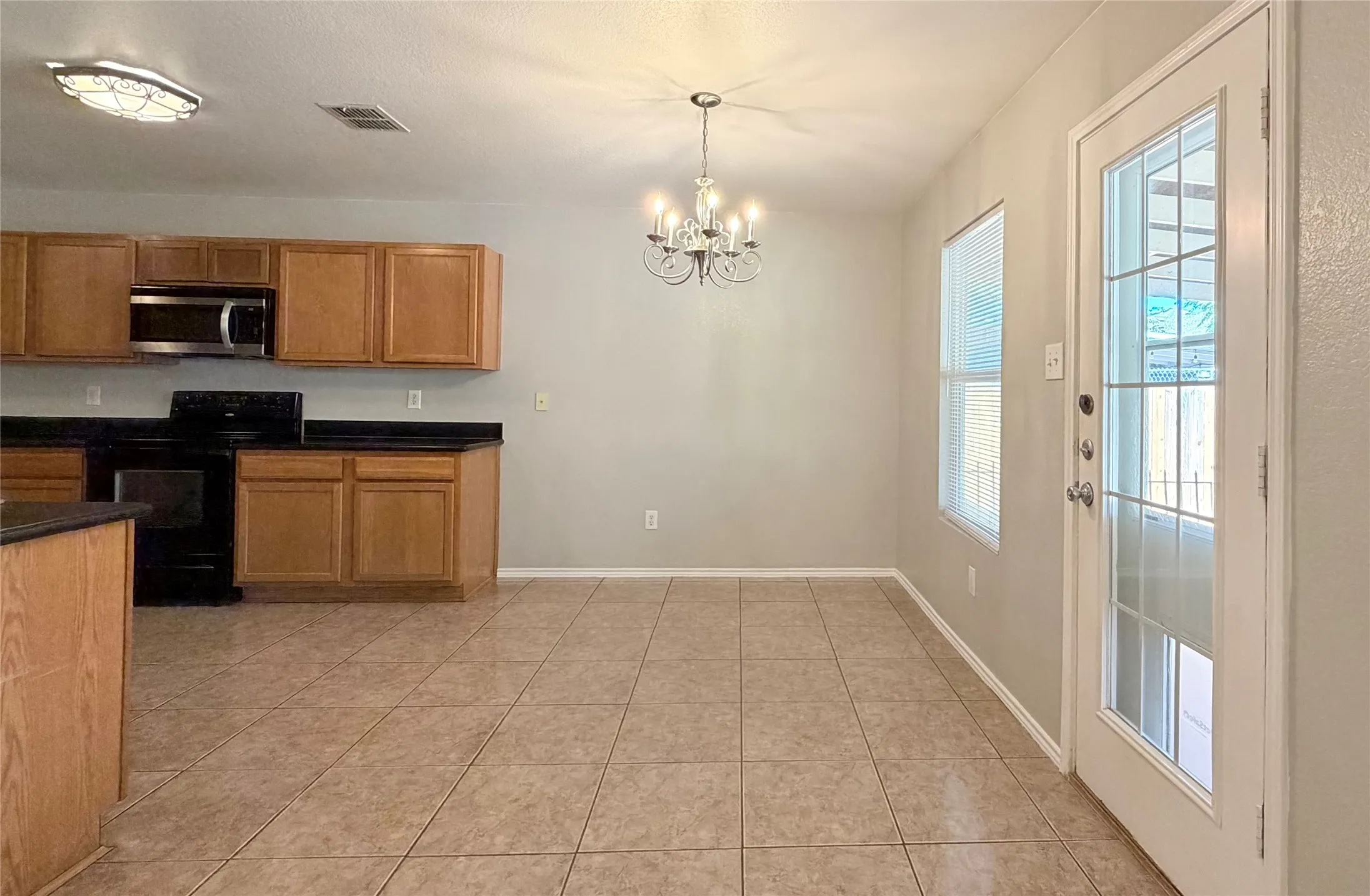 Kitchen and dining area featuring tile flooring, wood-finish cabinetry, black countertops, and a glass-paneled exterior door- Breakfast nook