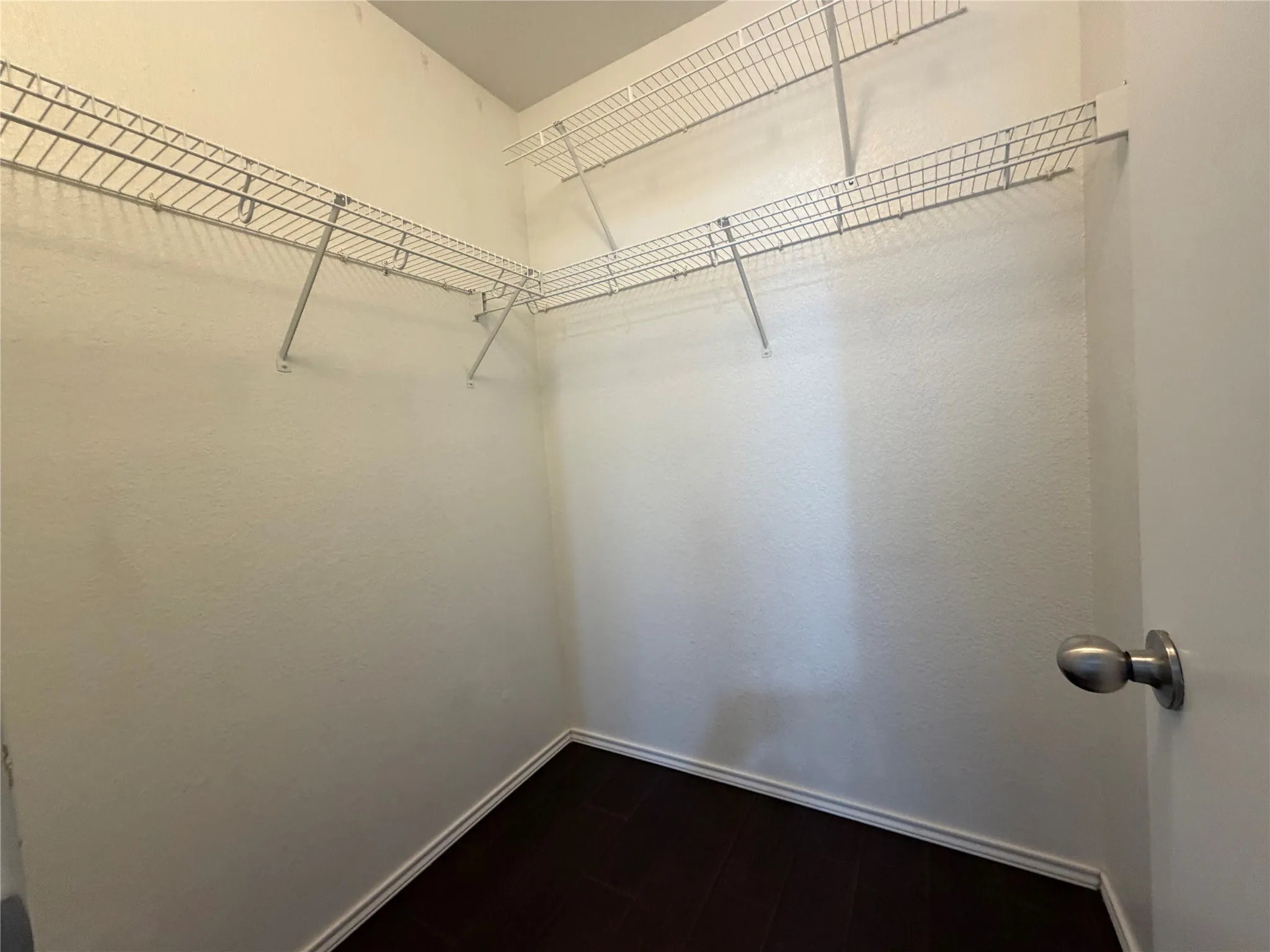 Bedroom upstairs with walk-in closet featuring wire shelving and dark wood-finish flooring