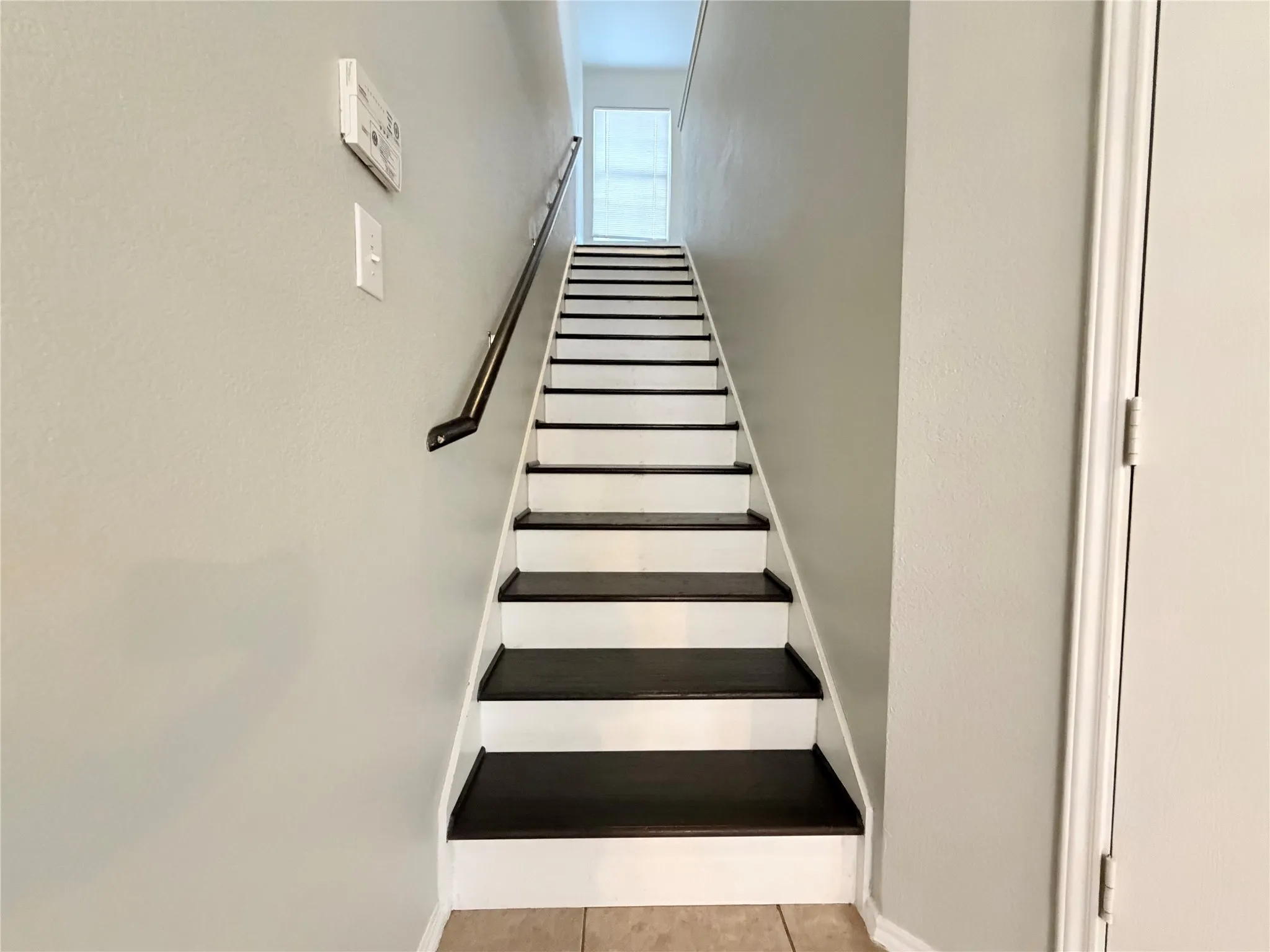 Staircase with dark-finish treads and white risers, featuring a black handrail and light neutral wall paint