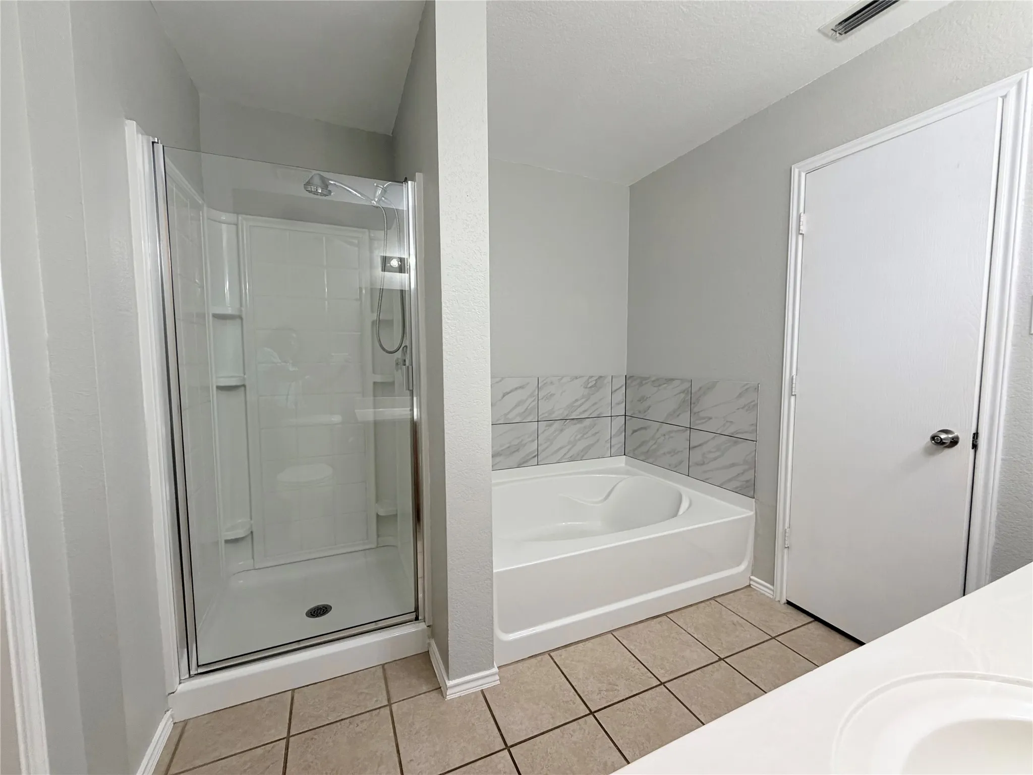Shower enclosure with glass door, separate soaking tub with tile surround, and neutral tile flooring