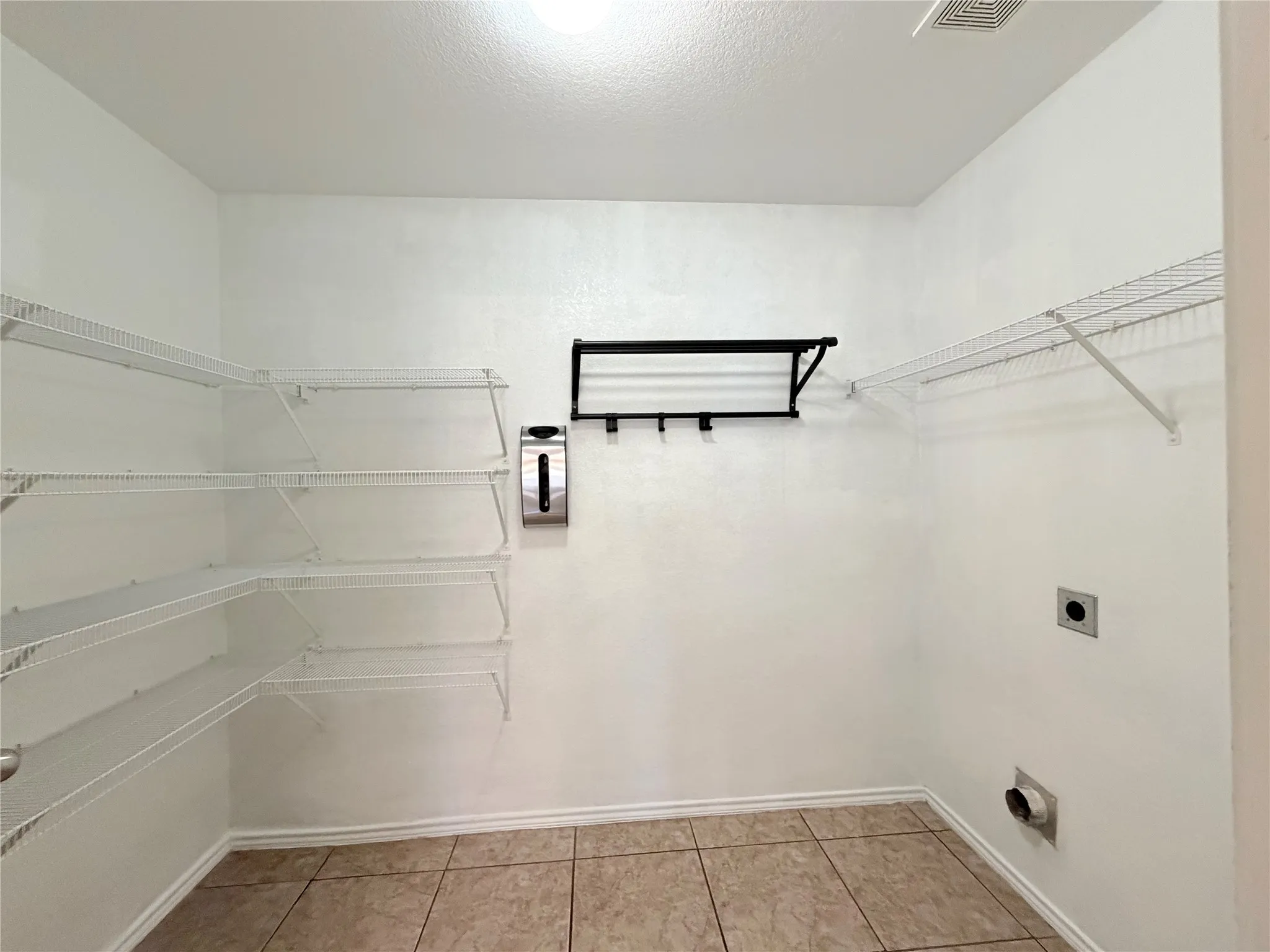 Tile flooring, white wire shelving, wall-mounted drying rack, wall-mounted soap dispenser, and white walls