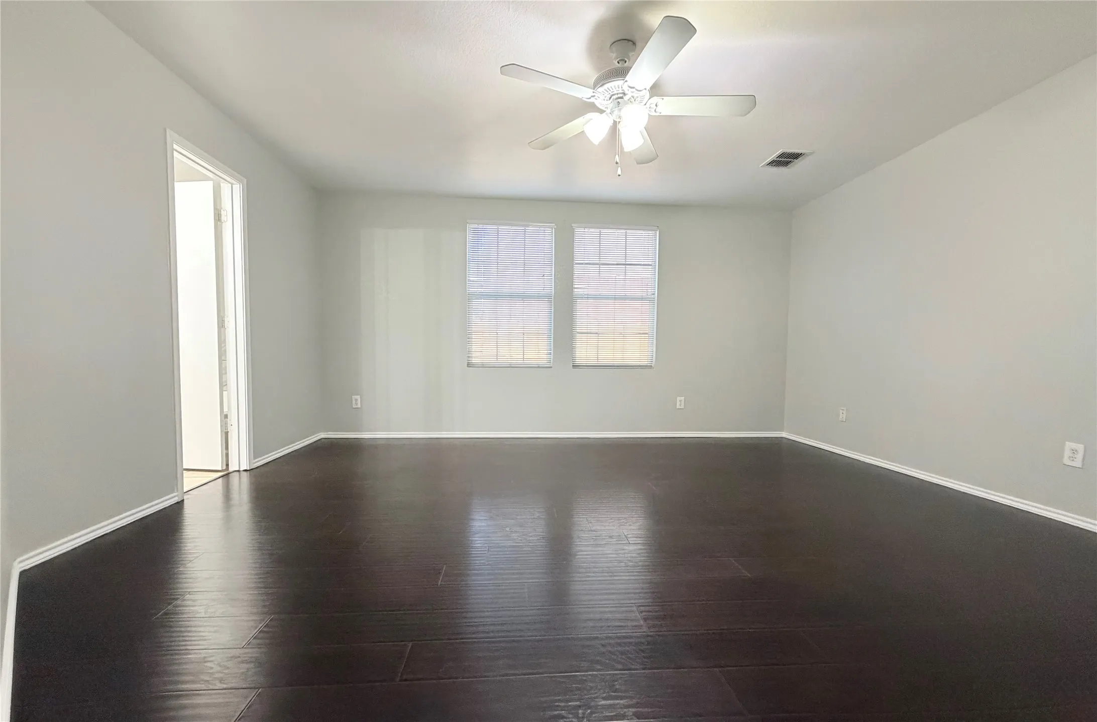 Spacious master room with dark wood-finish flooring, two windows, and a ceiling fan
