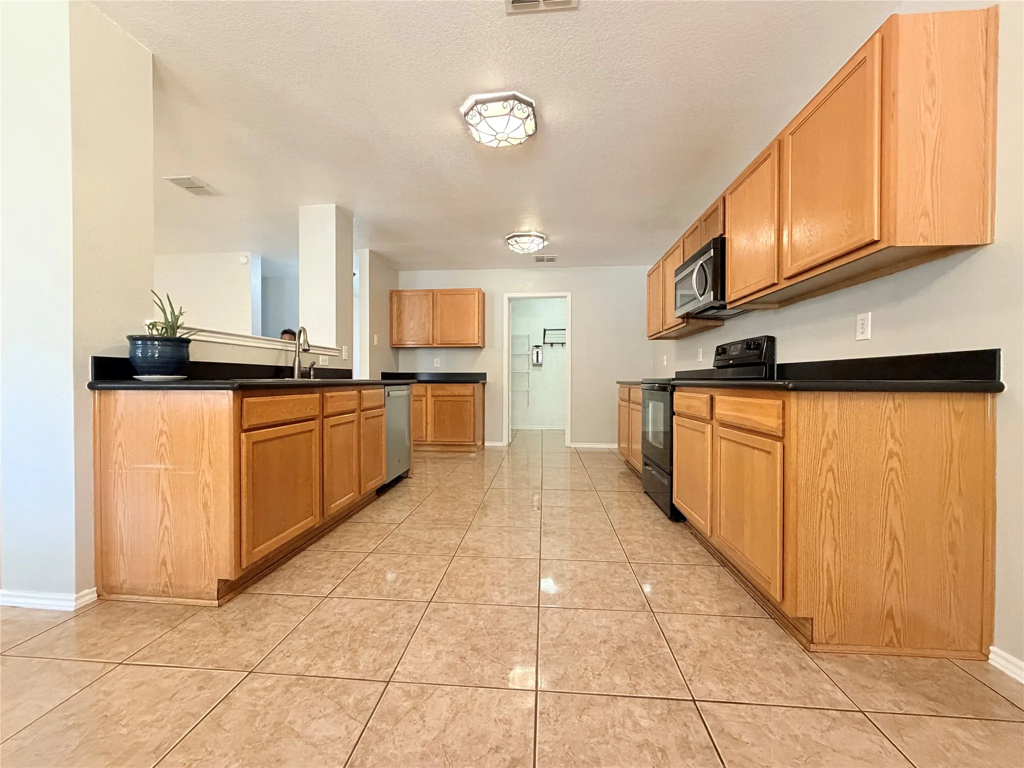 Kitchen featuring wood cabinetry, dark countertops, built-in microwave, dishwasher, and tile flooring