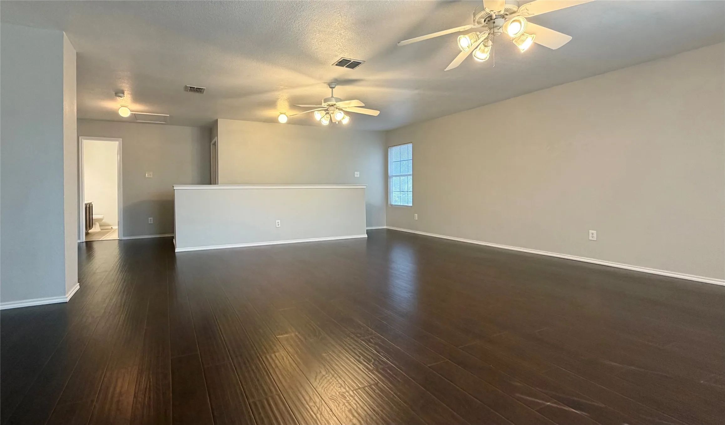 Game room/living room featuring wood-finish flooring, light neutral wall paint, multiple ceiling fans with integrated lighting, and natural light from a window