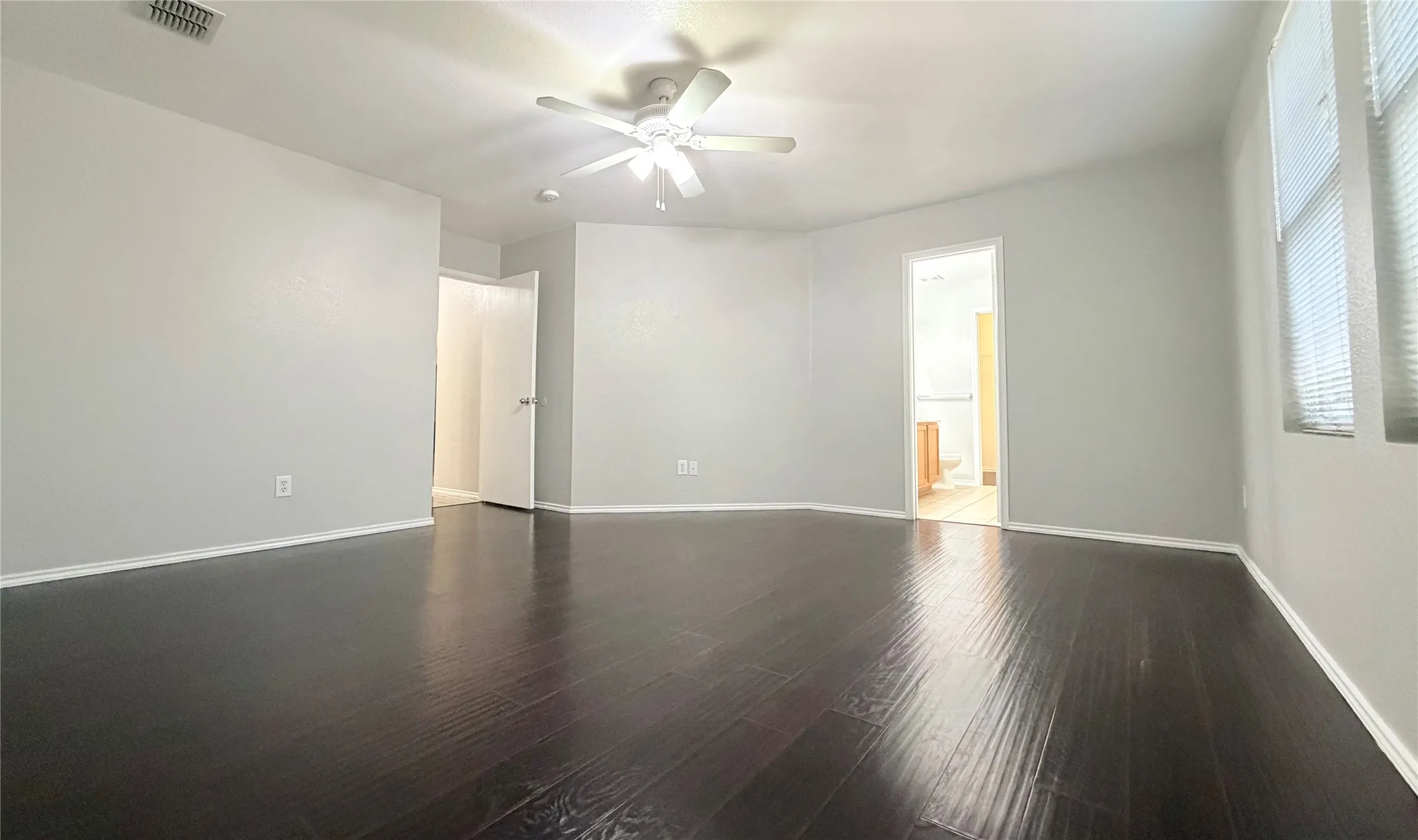 Spacious master room featuring dark wood-finish flooring, light-toned walls, and a ceiling fan