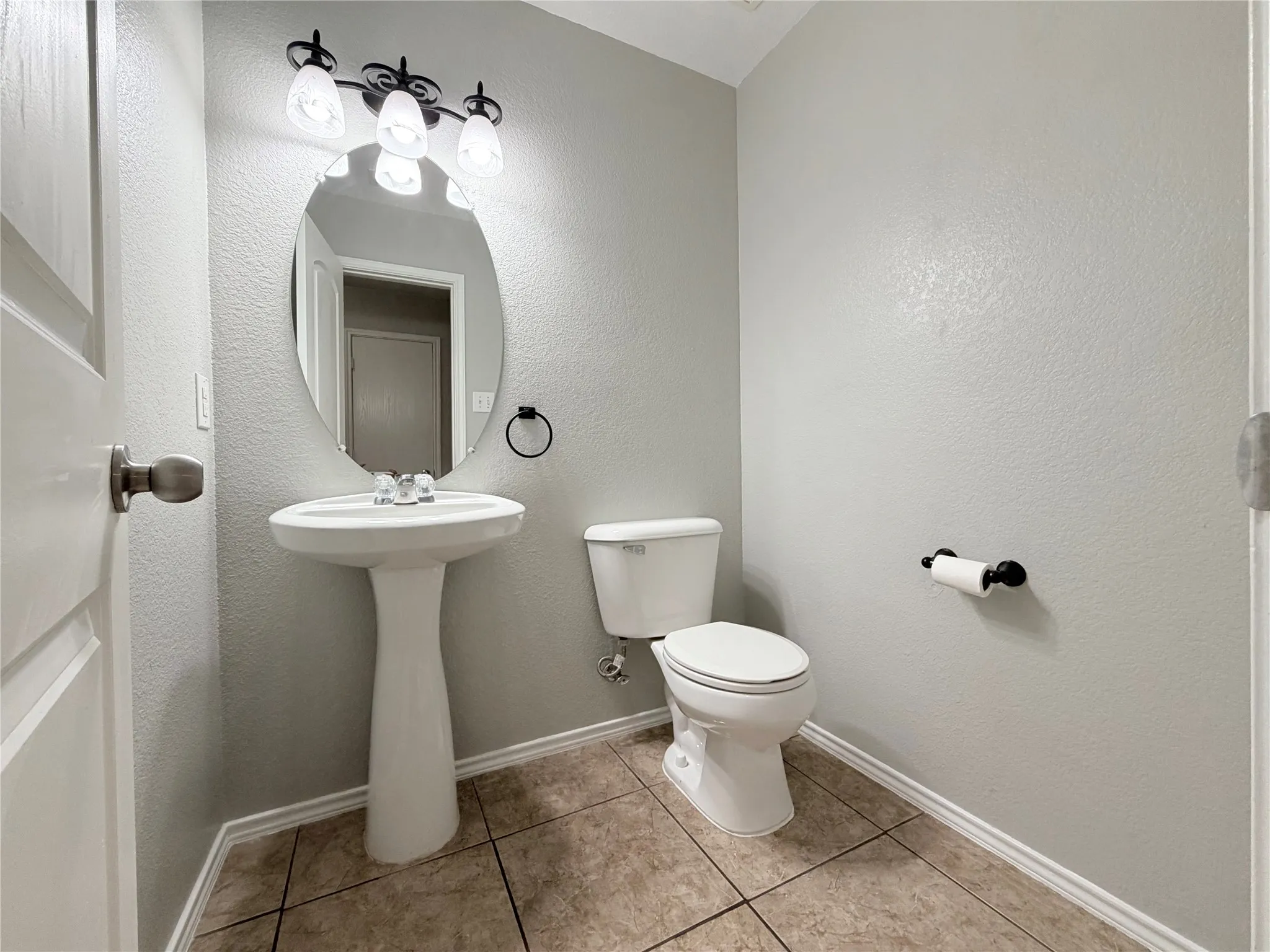 Pedestal sink with chrome faucet, oval mirror, and three-bulb vanity light fixture