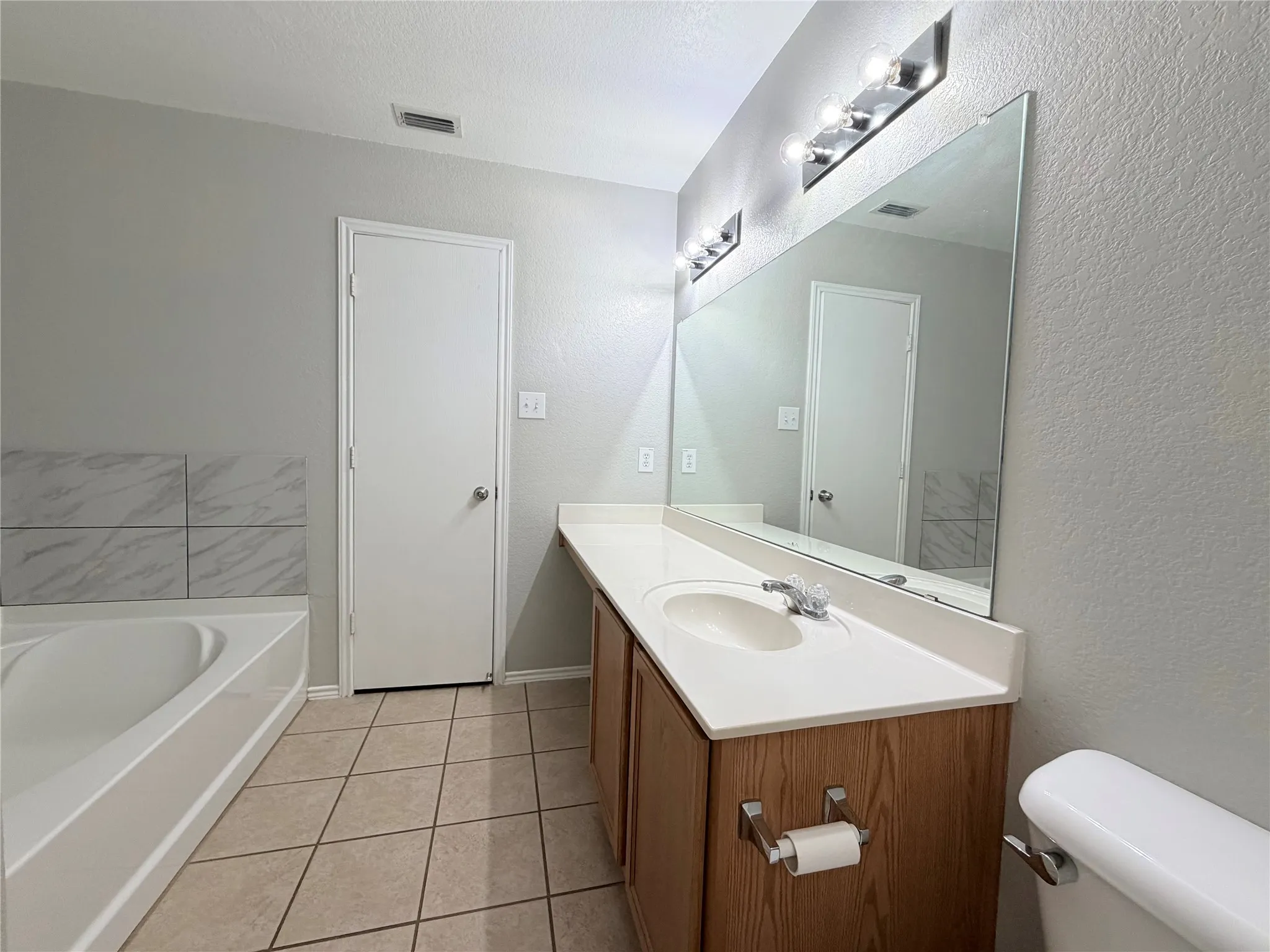 Vanity with a single basin sink, large wall-mounted mirror, and overhead strip lighting