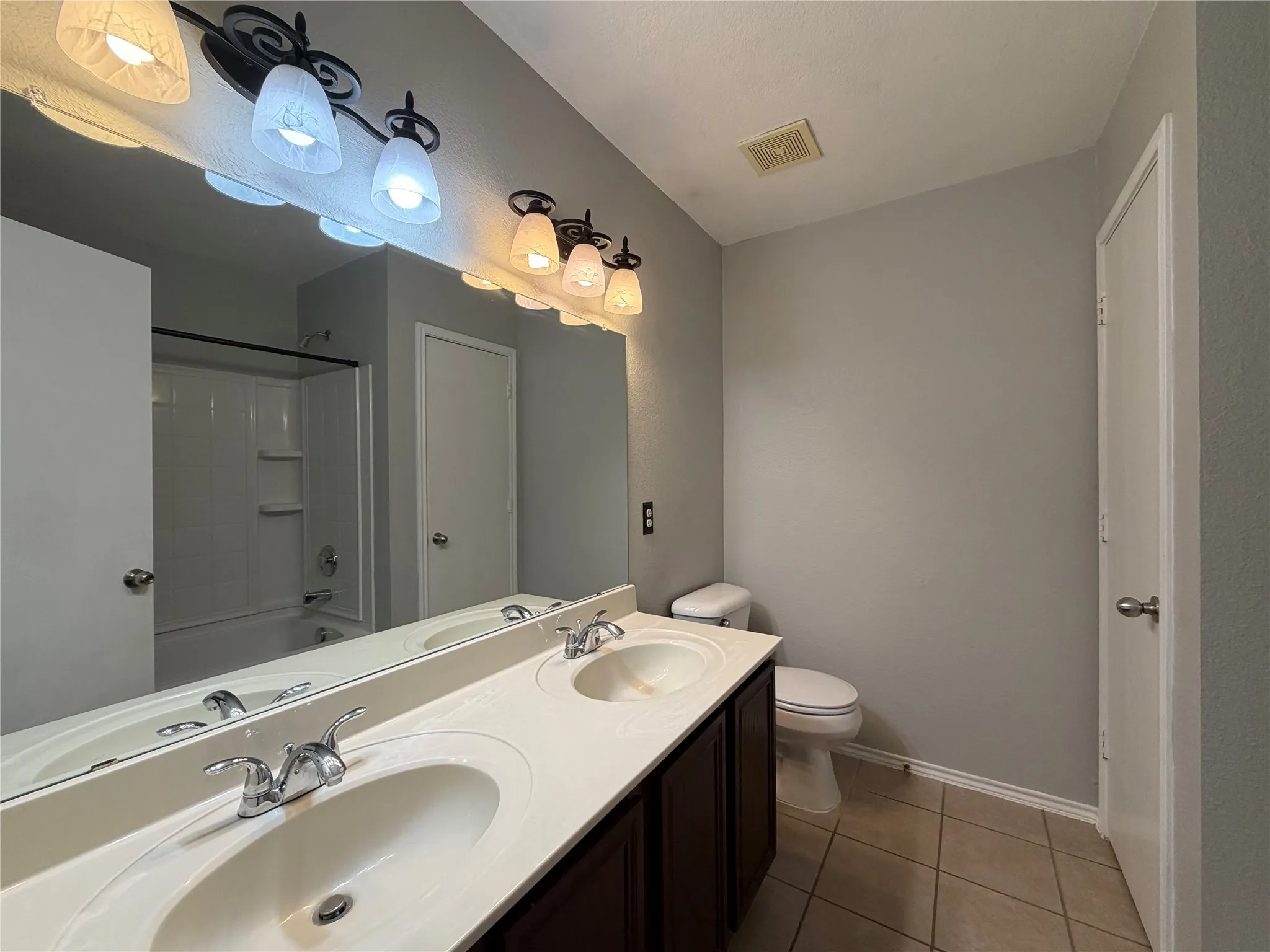 Double vanity with integrated sinks, dark wood-finish cabinetry, a large wall-mounted mirror, and tile flooring