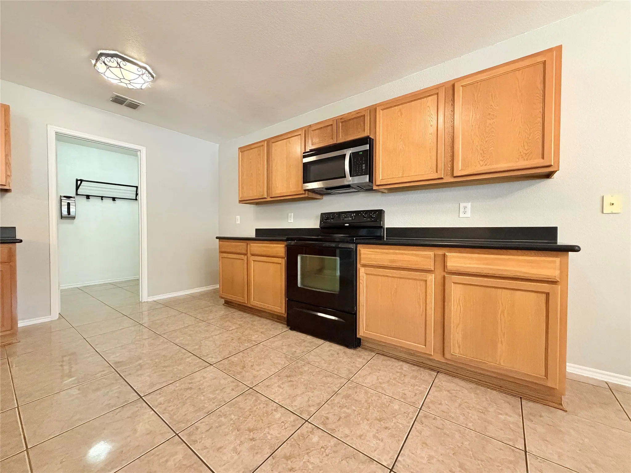 Kitchen featuring wood-finish cabinetry, black countertops, a black range, a stainless steel microwave, and tile flooring