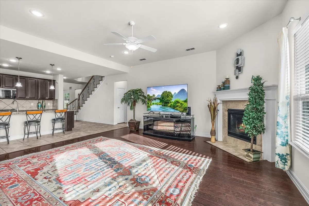 Spacious living area featuring wood-finish flooring, a fireplace with a stone surround, and a ceiling fan