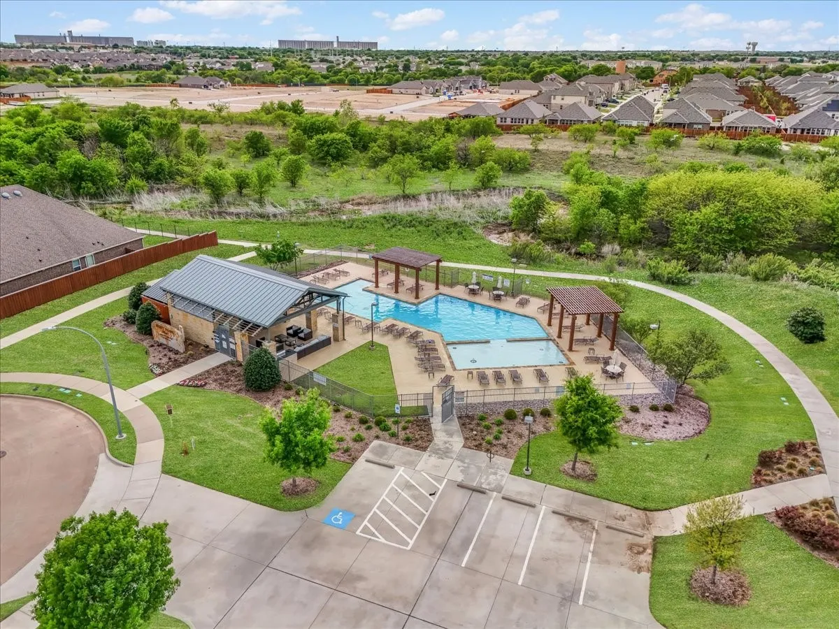 Community pool with multiple swimming areas, adjacent covered outdoor lounge, and surrounding green spaces