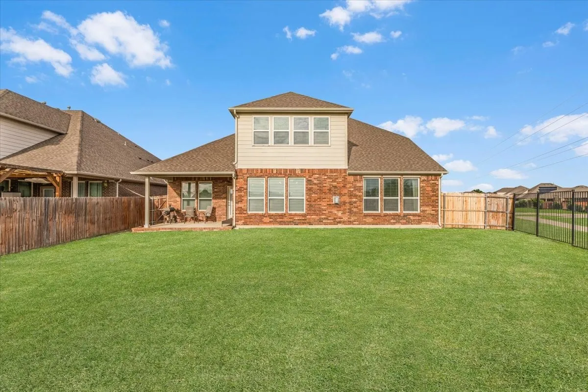 Expansive backyard with a manicured lawn, brick and siding exterior, a covered patio, and a combination of wood and metal fencing