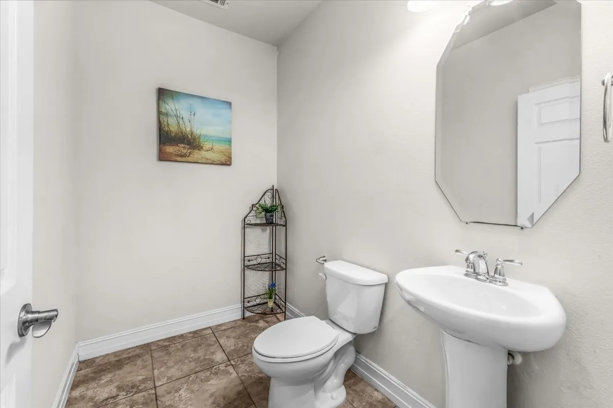Pedestal sink with chrome faucet, octagonal mirror, and ceramic tile flooring