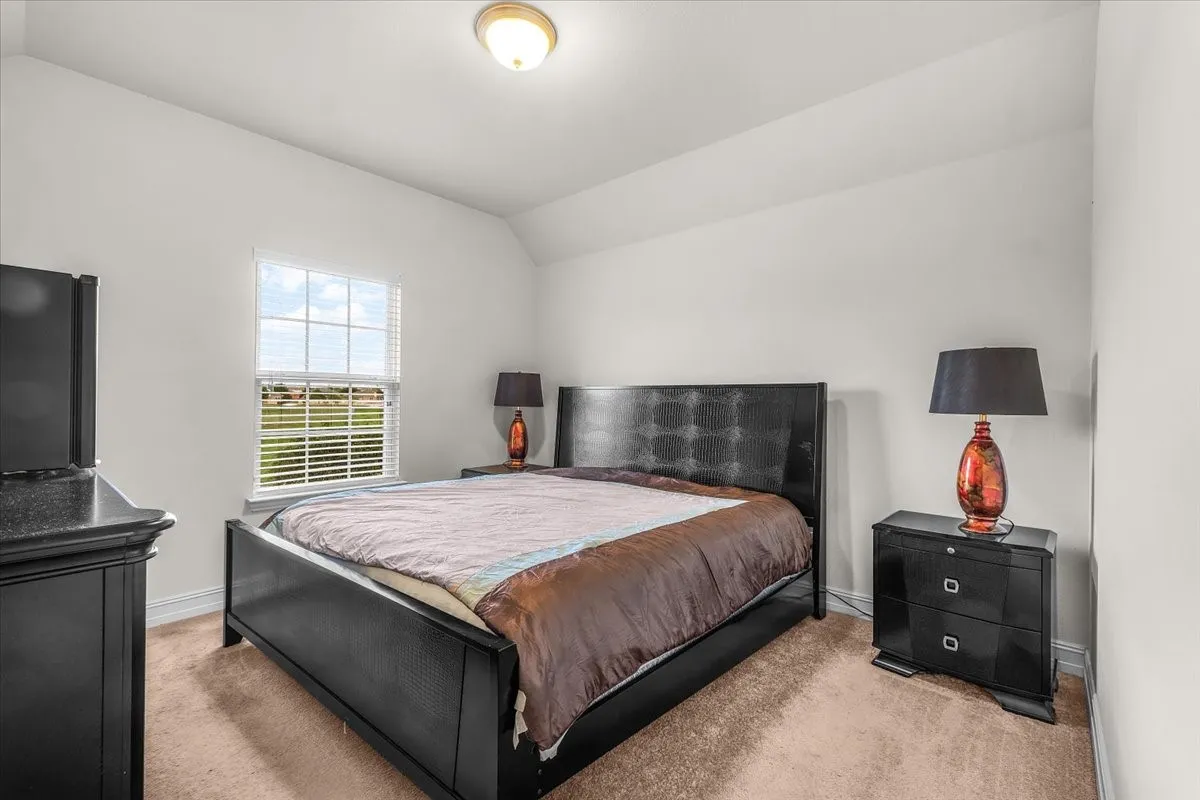 Spacious primary bedroom with black upholstered bed frame, neutral carpet flooring, and soft ambient lighting from ceiling fixture