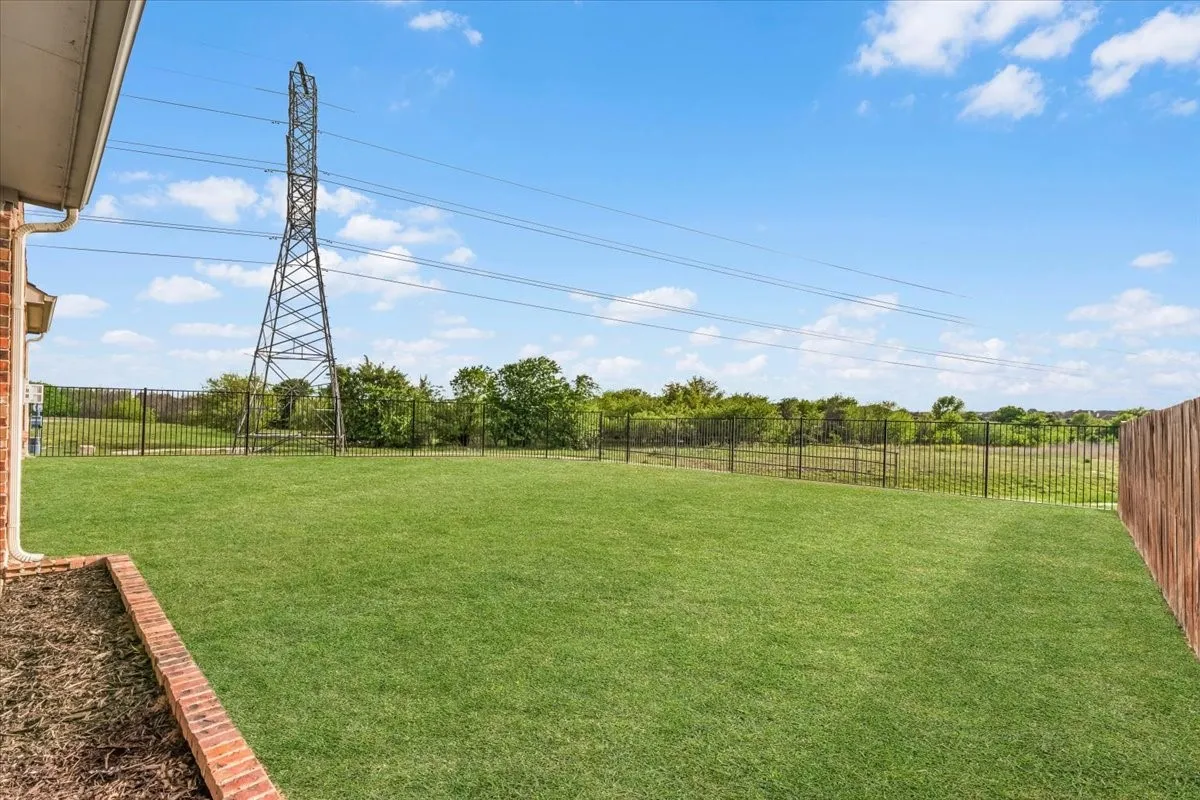 Expansive manicured lawn with mature tree line and metal fencing, anchored by a utility transmission tower