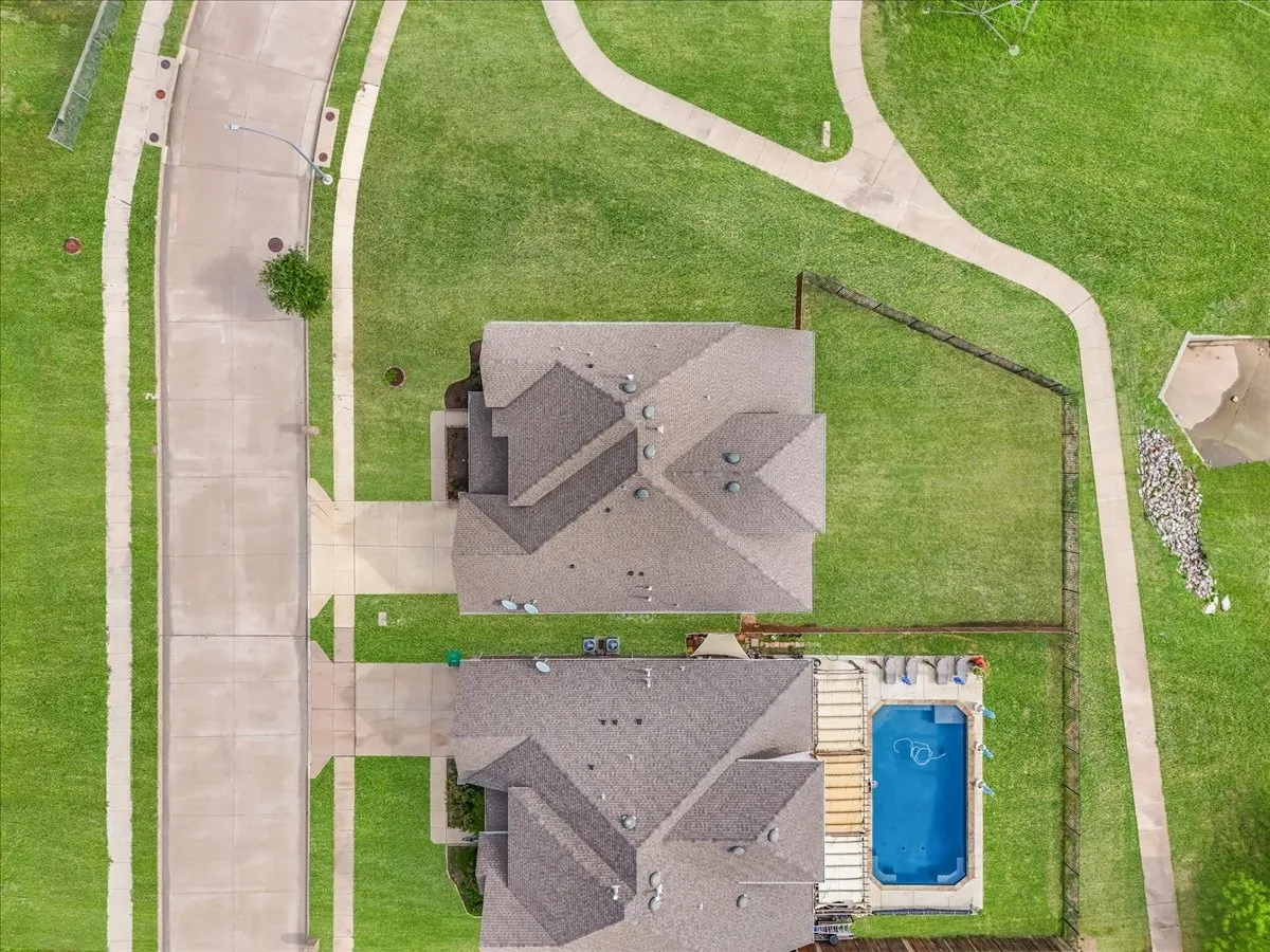 Rectangular swimming pool, concrete patio, fenced yard, asphalt shingle roofing, concrete driveway