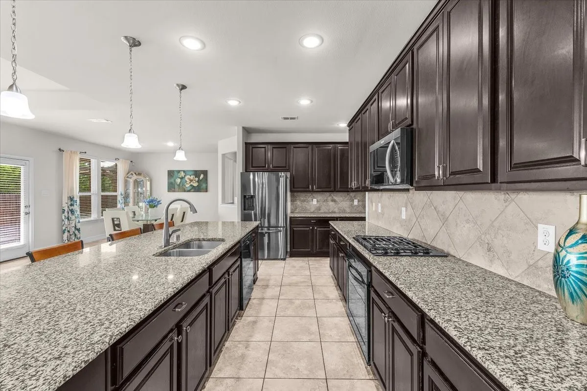 Kitchen featuring an expansive island with an undermount sink, dark wood cabinetry, granite countertops, a gas cooktop, and tile flooring