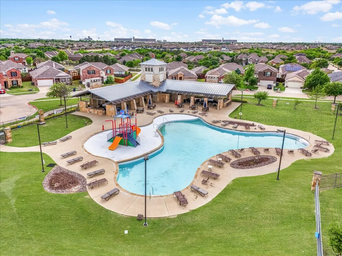 Resort-style pool with integrated water play structure, expansive paved sundeck, and stone-clad open-air cabana with a metal roof
