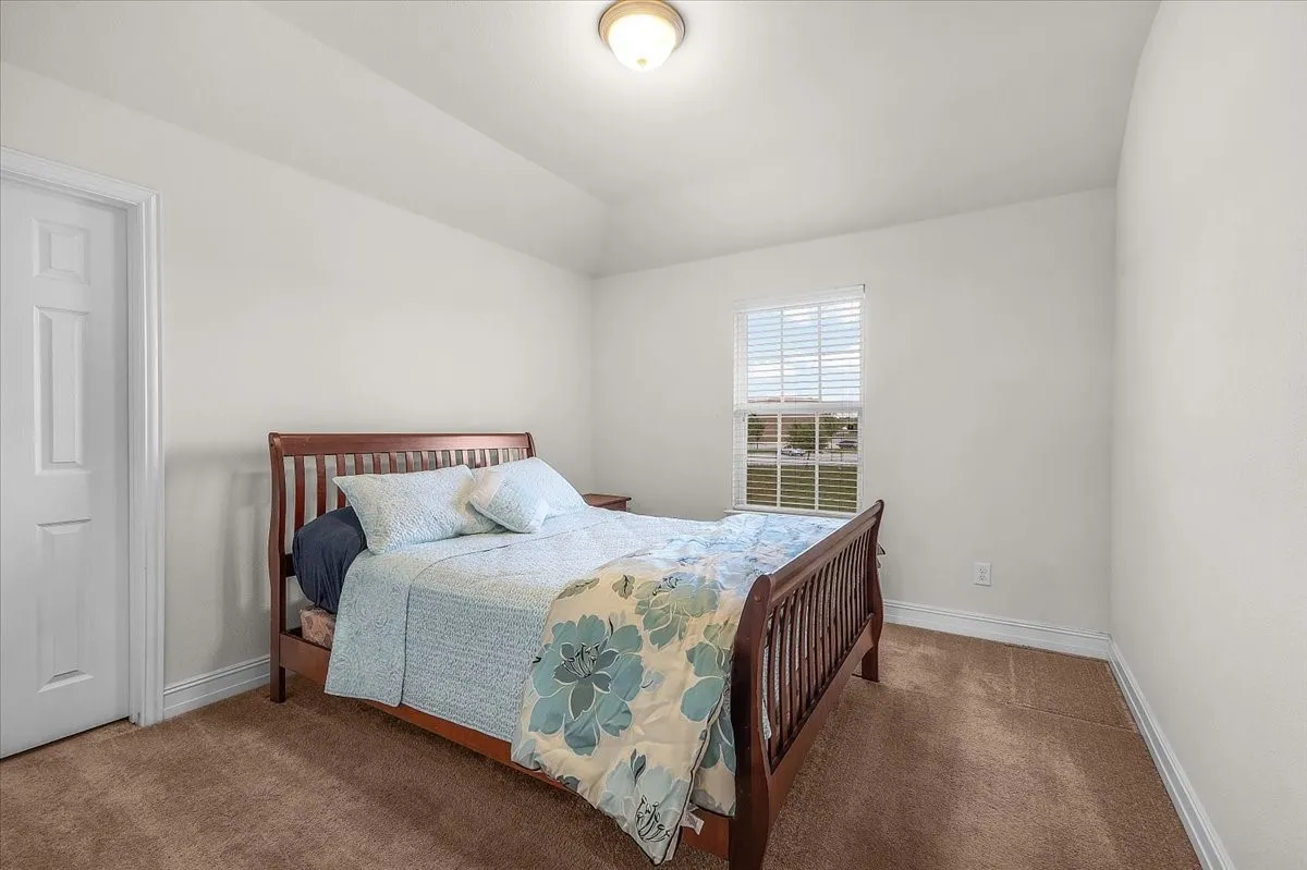 Vaulted ceiling, white walls, textured carpeting, window with blinds, and a paneled door