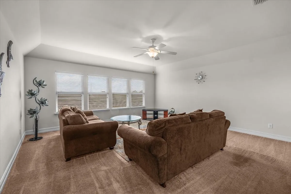 Carpeted room featuring multiple windows with blinds, a ceiling fan with integrated lighting, and white wall finishes