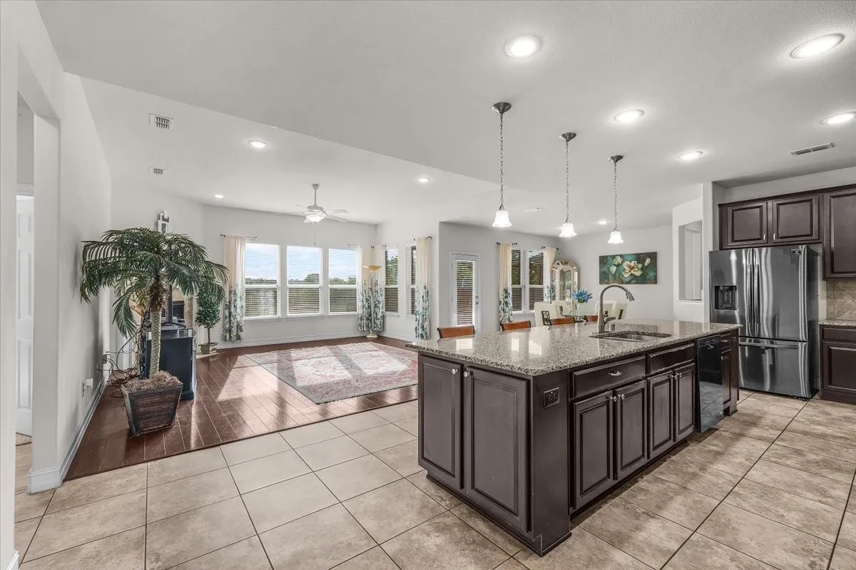 Open-concept living space with a kitchen island featuring a granite countertop, recessed lighting, wood-finish flooring, and a bank of windows