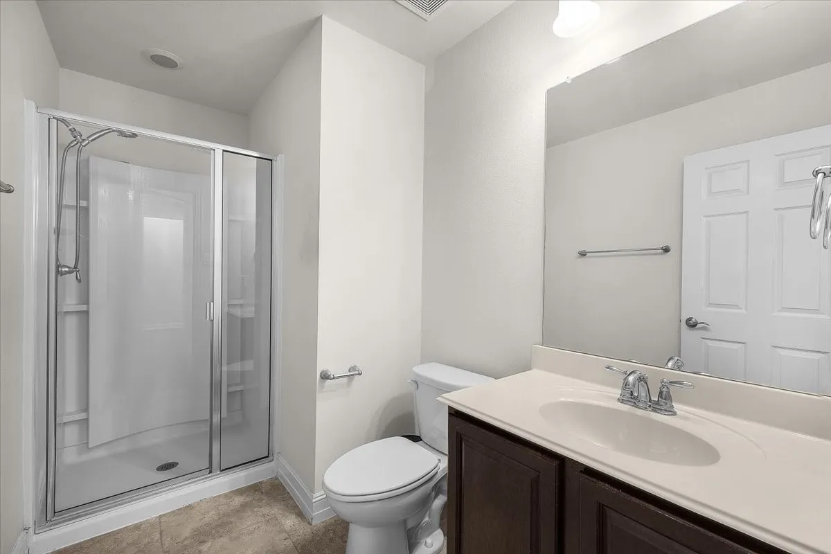 Bathroom featuring a glass-enclosed shower, a vanity with an integrated sink and base cabinetry, a full-width wall mirror, and tile flooring