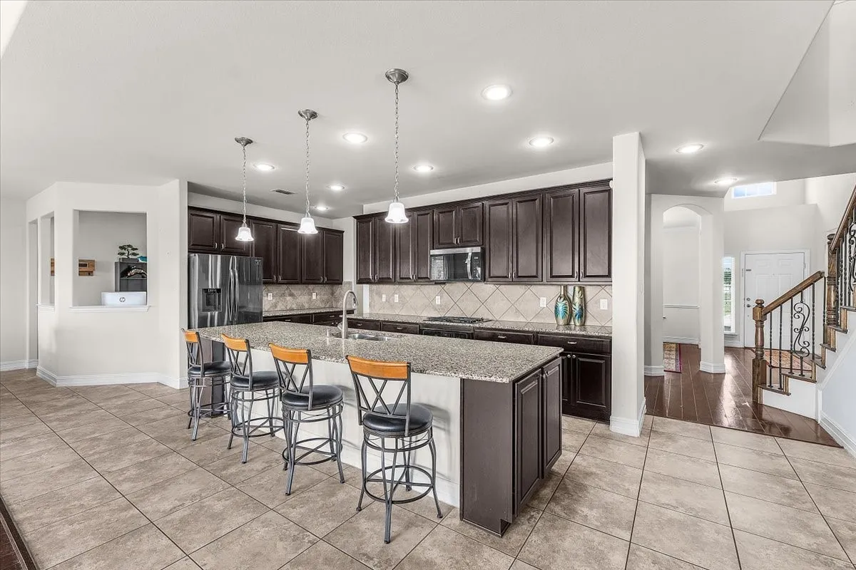 Gourmet kitchen with an expansive granite island, dark wood-finish cabinetry, stainless steel appliances, and pendant lighting