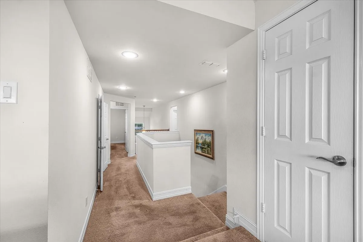 Recessed ceiling lighting, white painted walls, white trim work, brown carpeted flooring, and a white panel door with dark hardware