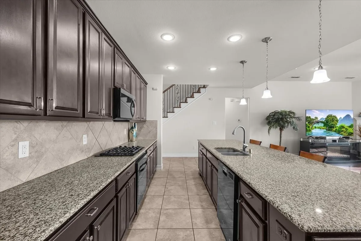 Kitchen featuring dark wood cabinetry, light granite countertops, a tiled backsplash, stainless steel appliances, and a central island with pendant lighting