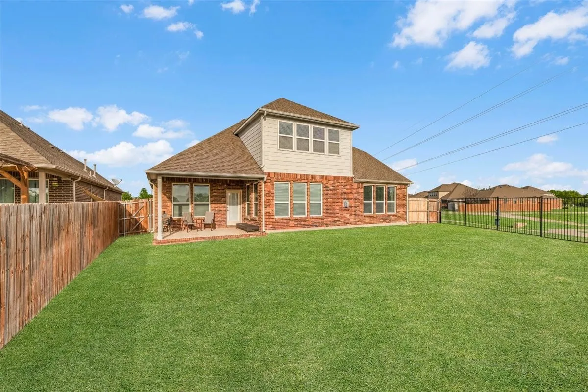 Expansive backyard featuring a covered patio, brick and siding exterior, multiple windows, and a combination of wood and wrought iron fencing
