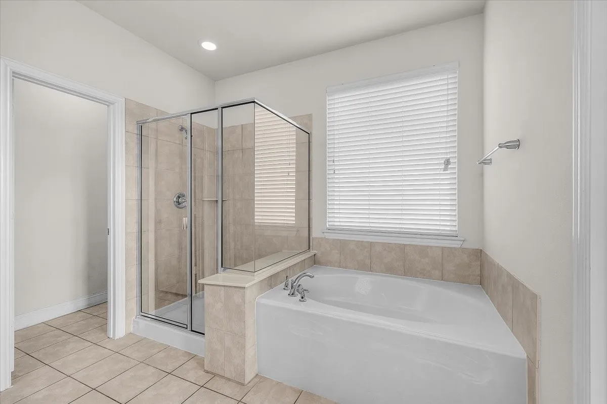 Tiled flooring with a glass-enclosed shower, built-in corner tub, and window with privacy blinds