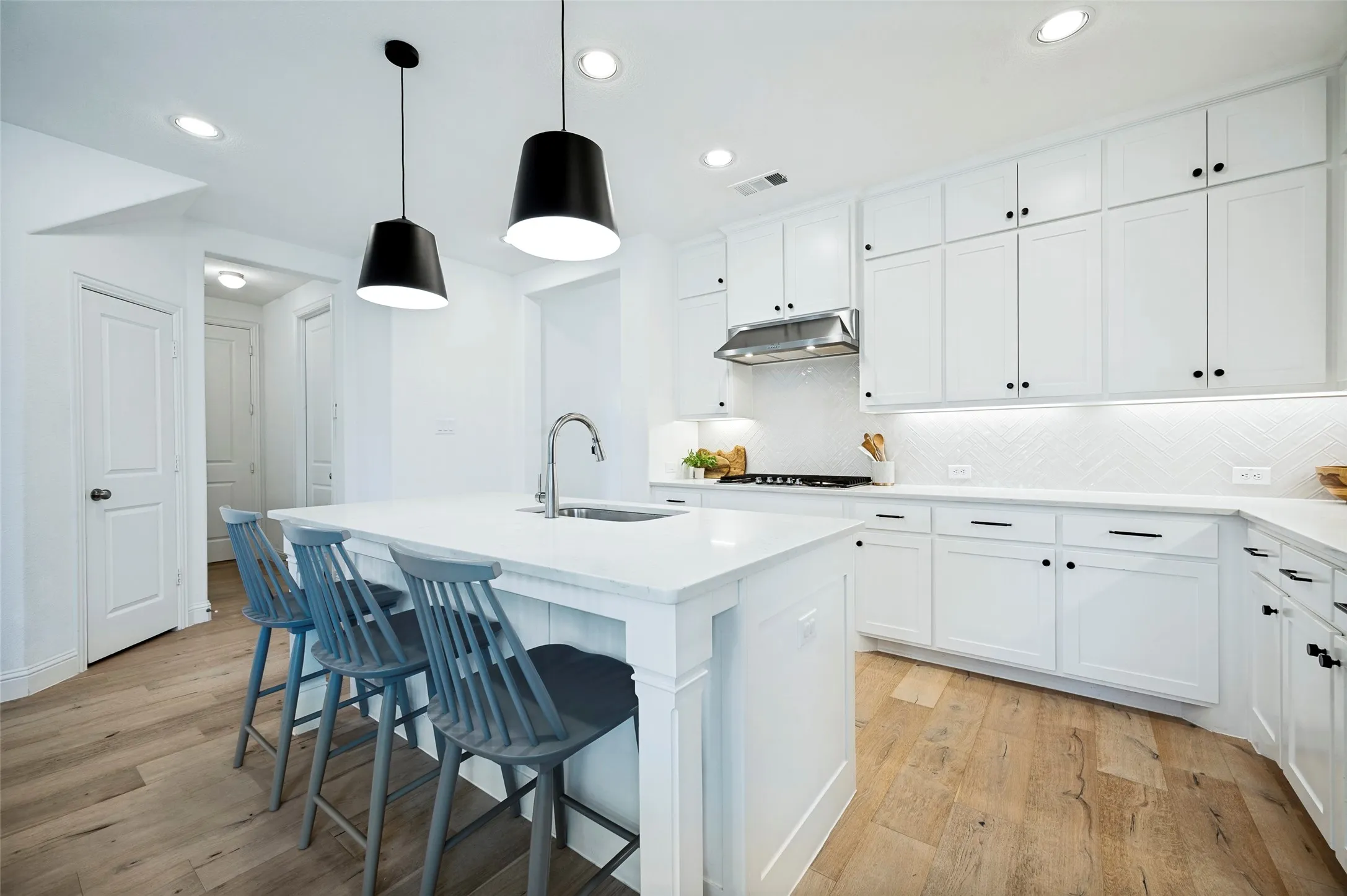 Kitchen featuring an island with a built-in sink, white cabinetry with dark hardware, a stainless steel range hood, and wood-finish flooring