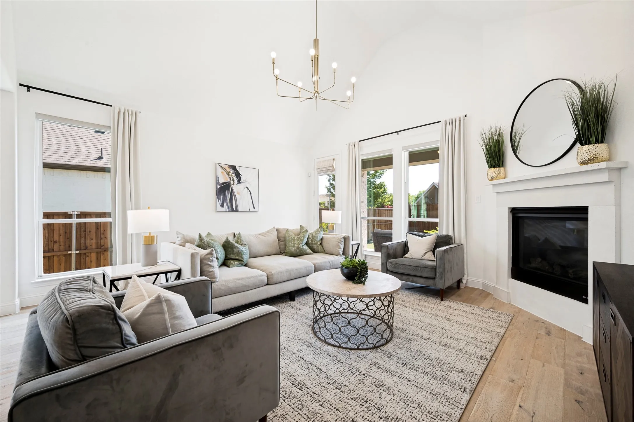 Vaulted ceilings, large windows, corner fireplace with a white mantel, wood-finish flooring, and a contemporary chandelier