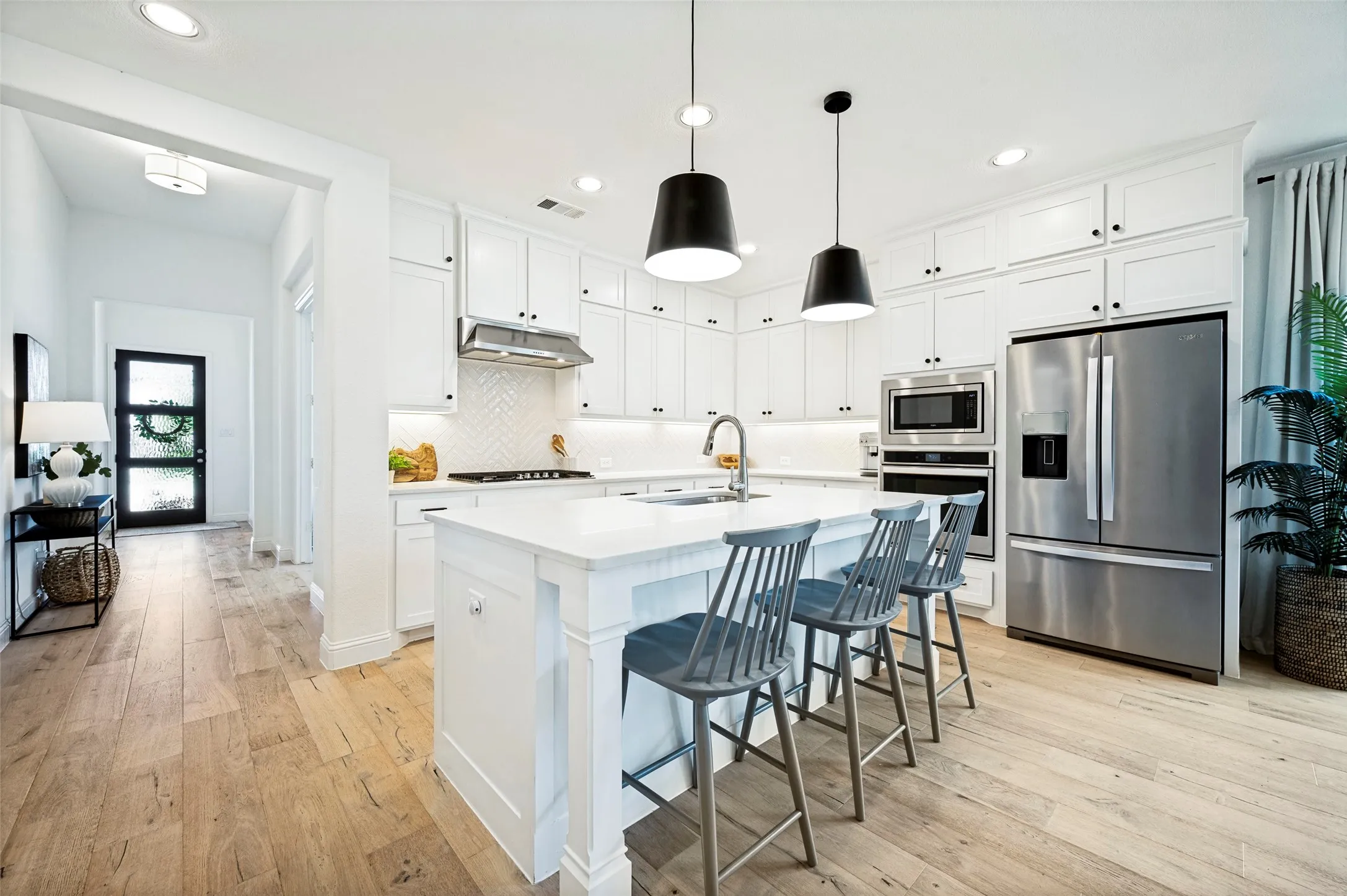 White shaker cabinetry, stainless steel appliances, kitchen island with seating, wood-finish flooring, and recessed lighting