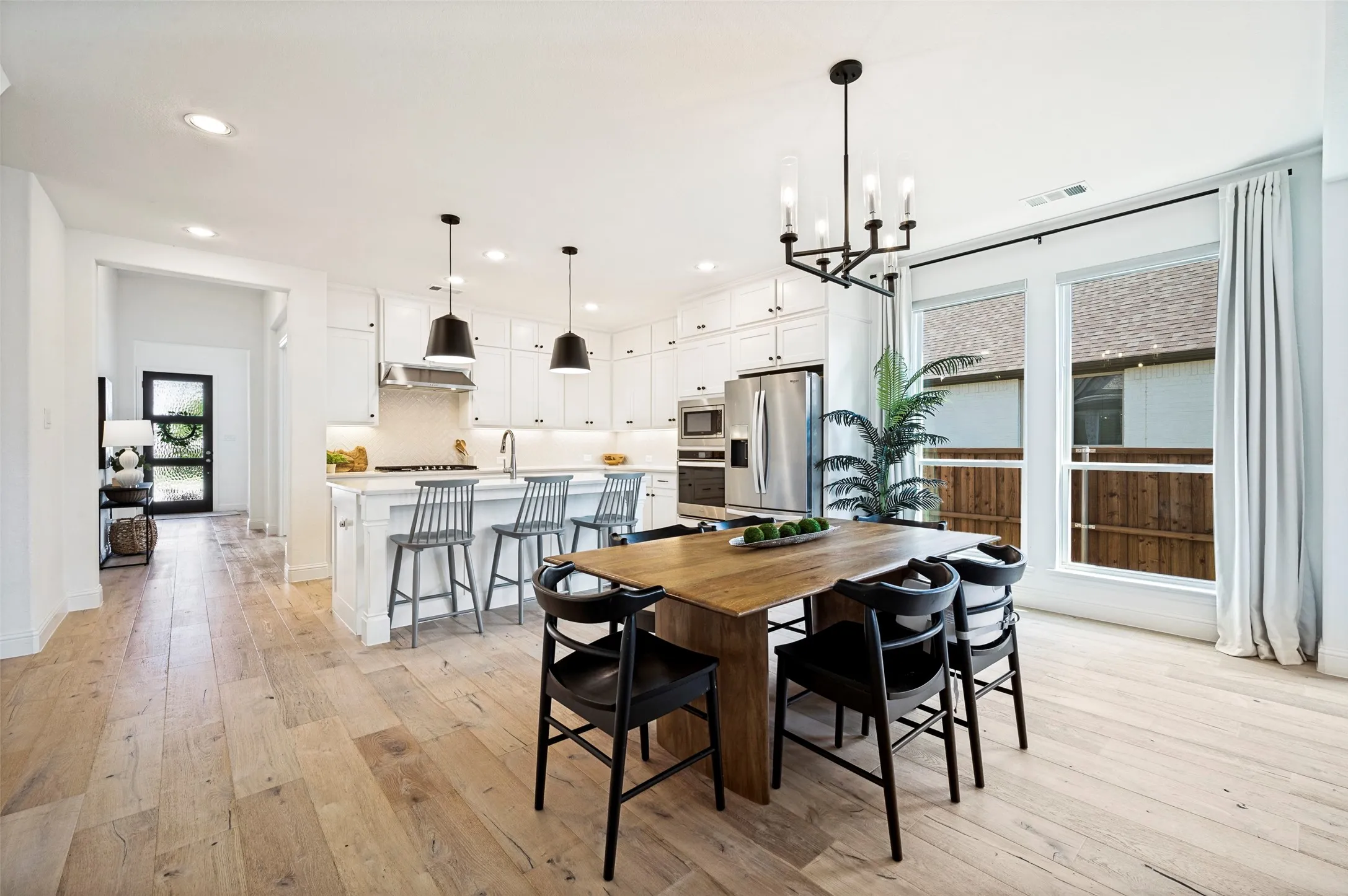 Open-concept living space with light wood-finish flooring, a contemporary chandelier, and a kitchen island with pendant lighting