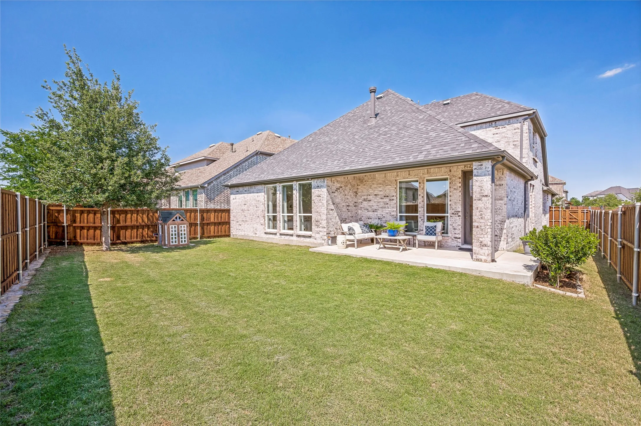 Expansive backyard featuring a manicured lawn, full privacy fencing, a covered concrete patio, and a brick exterior