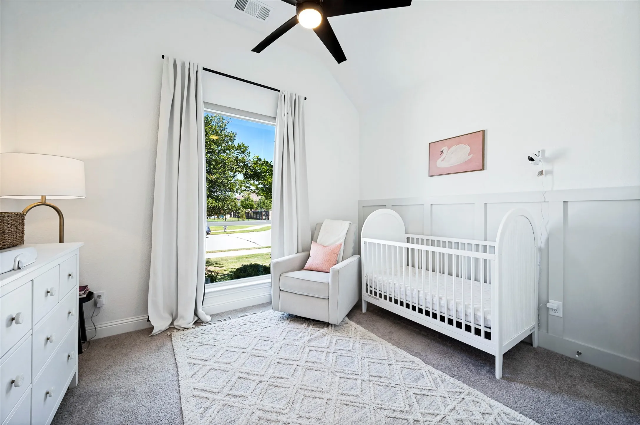 Vaulted ceiling with a ceiling fan, board and batten wall detailing, large window with outdoor landscaping, and carpeted flooring
