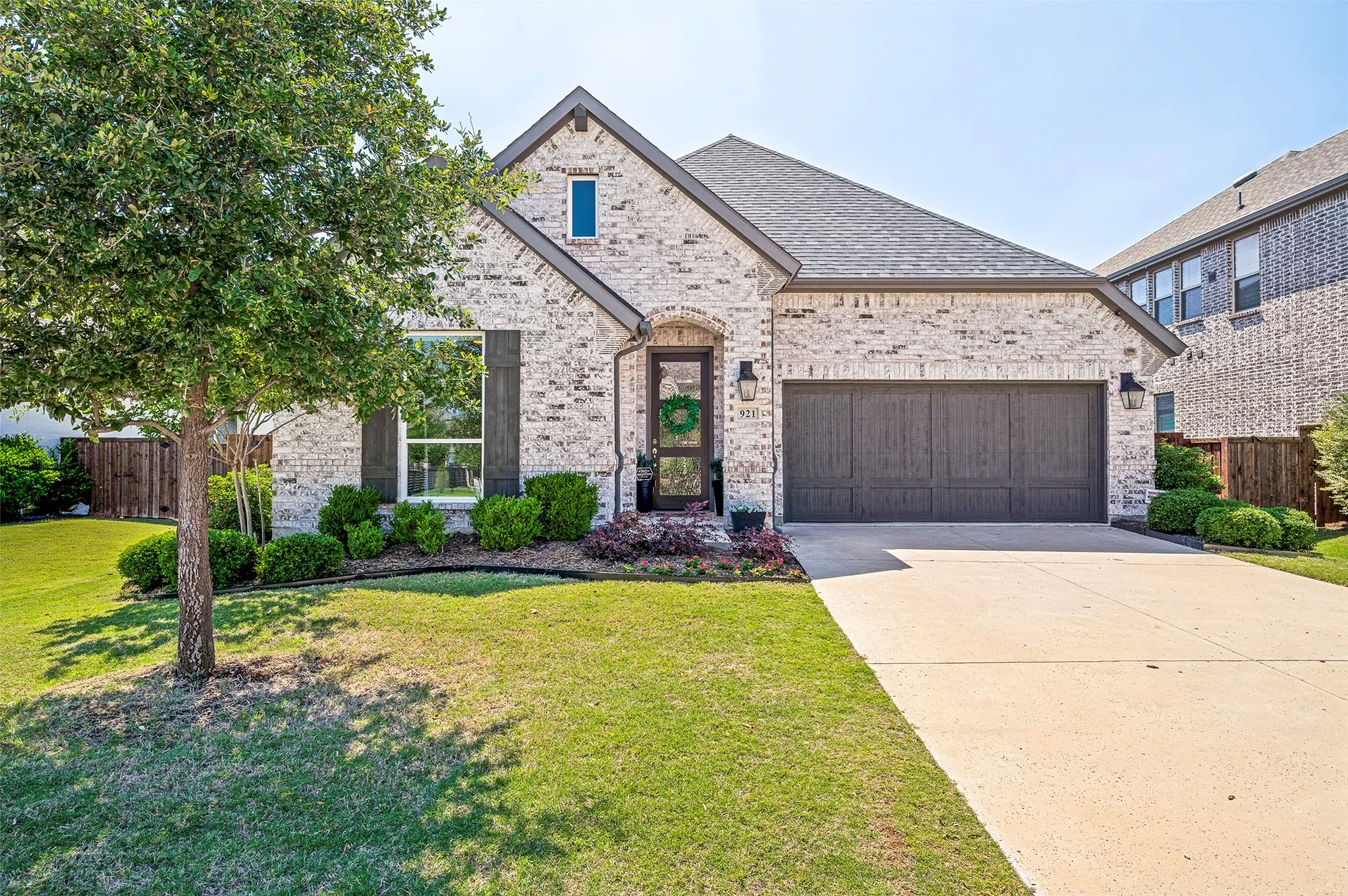 Brick exterior with gray-toned accents, attached garage with a dark wood-finish door, covered entry, and manicured landscaping