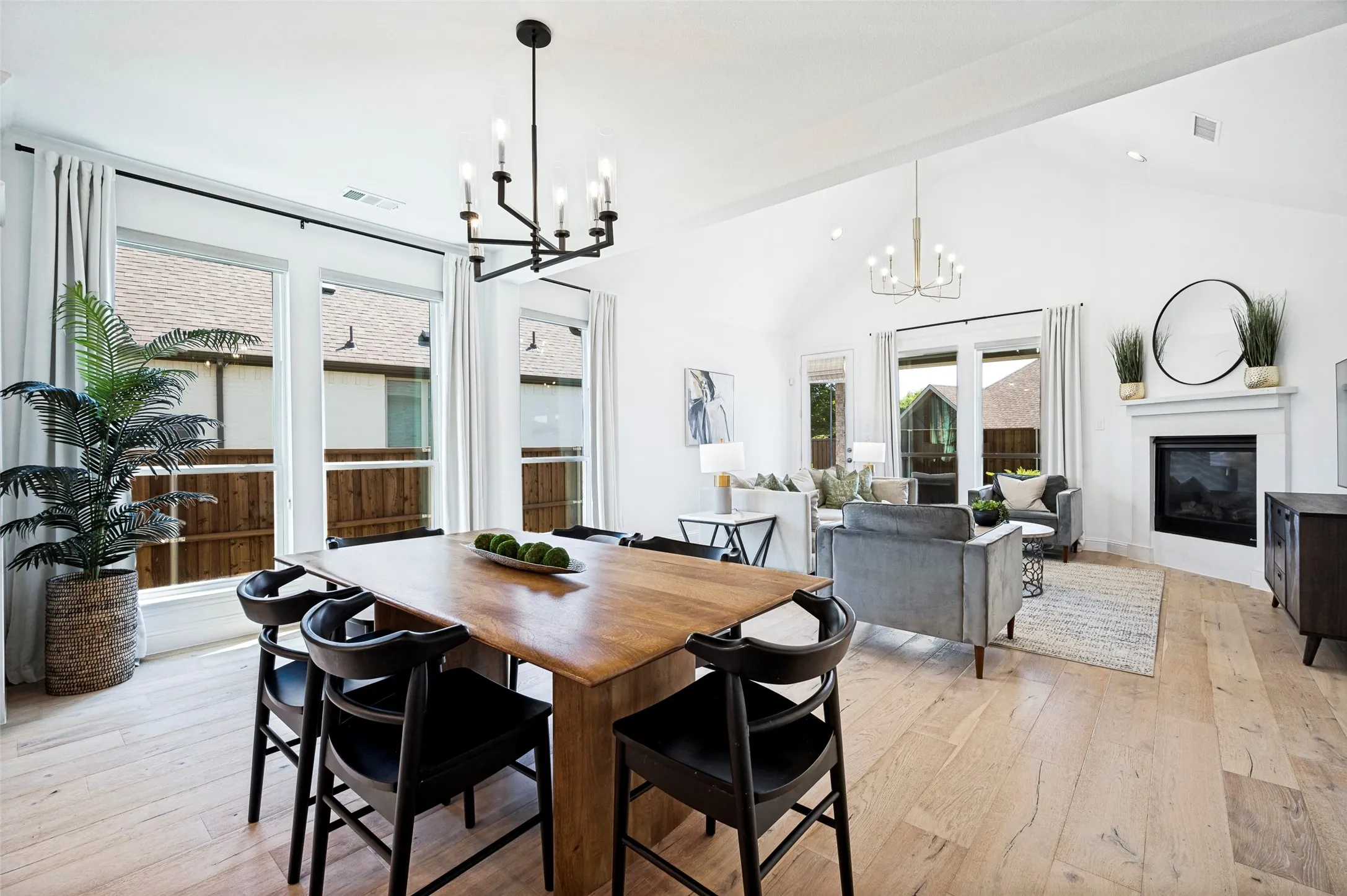 Open-concept living space featuring wood-finish flooring, a fireplace with a white mantel, and a vaulted ceiling