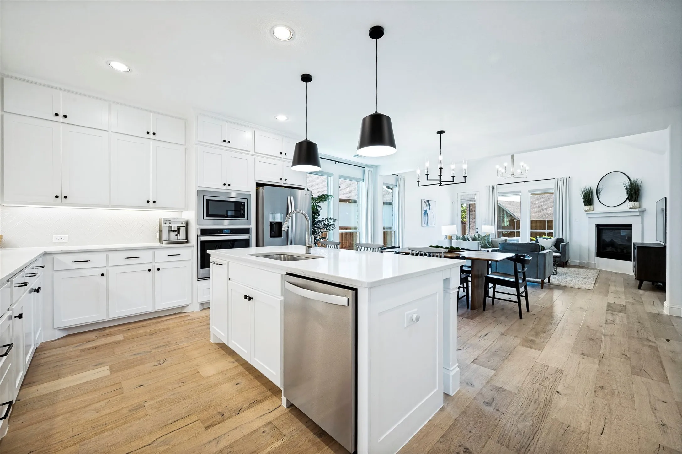 Open-concept living space featuring wood-finish flooring, a kitchen island with integrated sink, stainless steel appliances, white cabinetry, and a fireplace