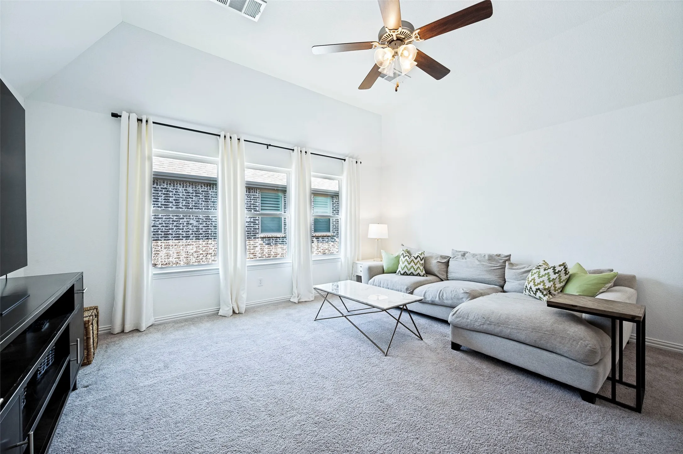 Vaulted ceiling, ceiling fan with integrated lighting, multiple windows, and light-colored carpeting