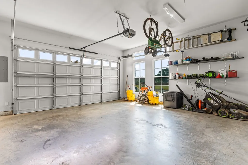 Attached two-car garage featuring a concrete floor, two windows, and built-in wall shelving