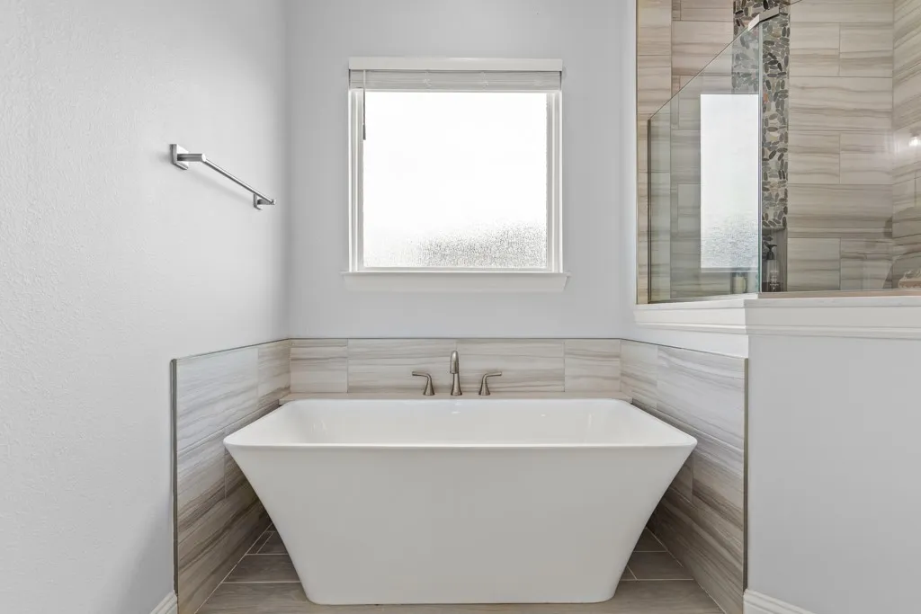 Freestanding soaking tub with polished chrome fixtures, tile surround, and an adjacent glass-enclosed shower with a textured tile accent wall