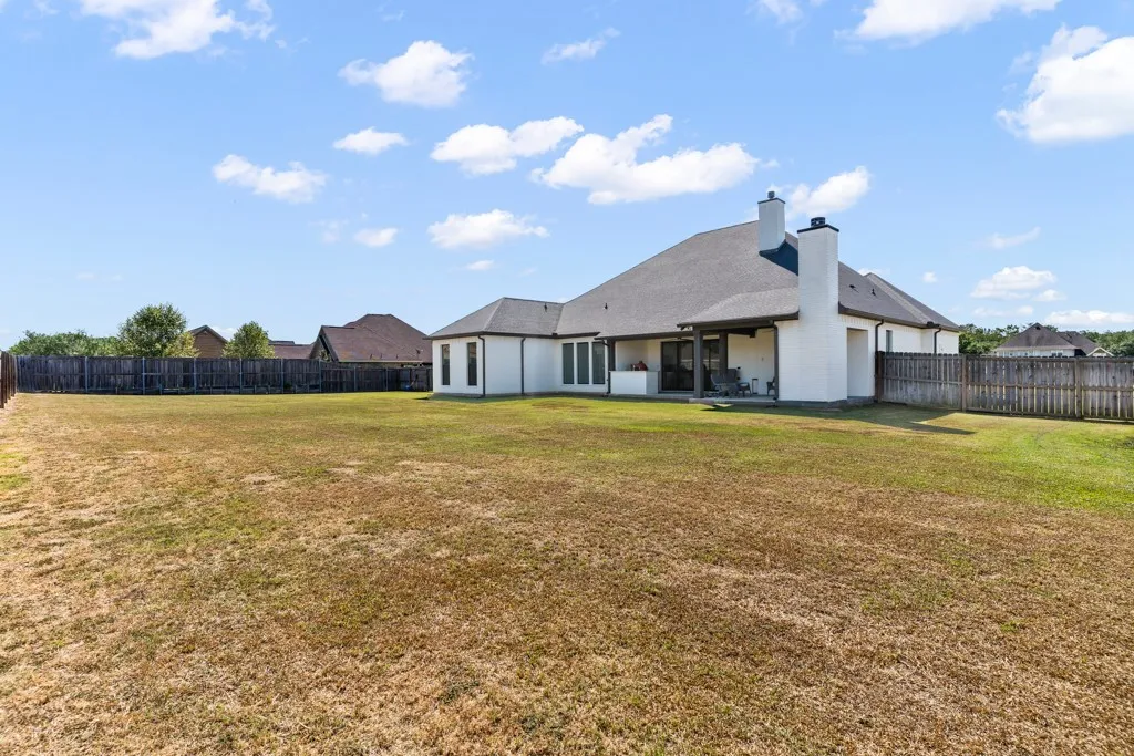 Expansive backyard with a full perimeter fence, covered patio, and multi-pane windows