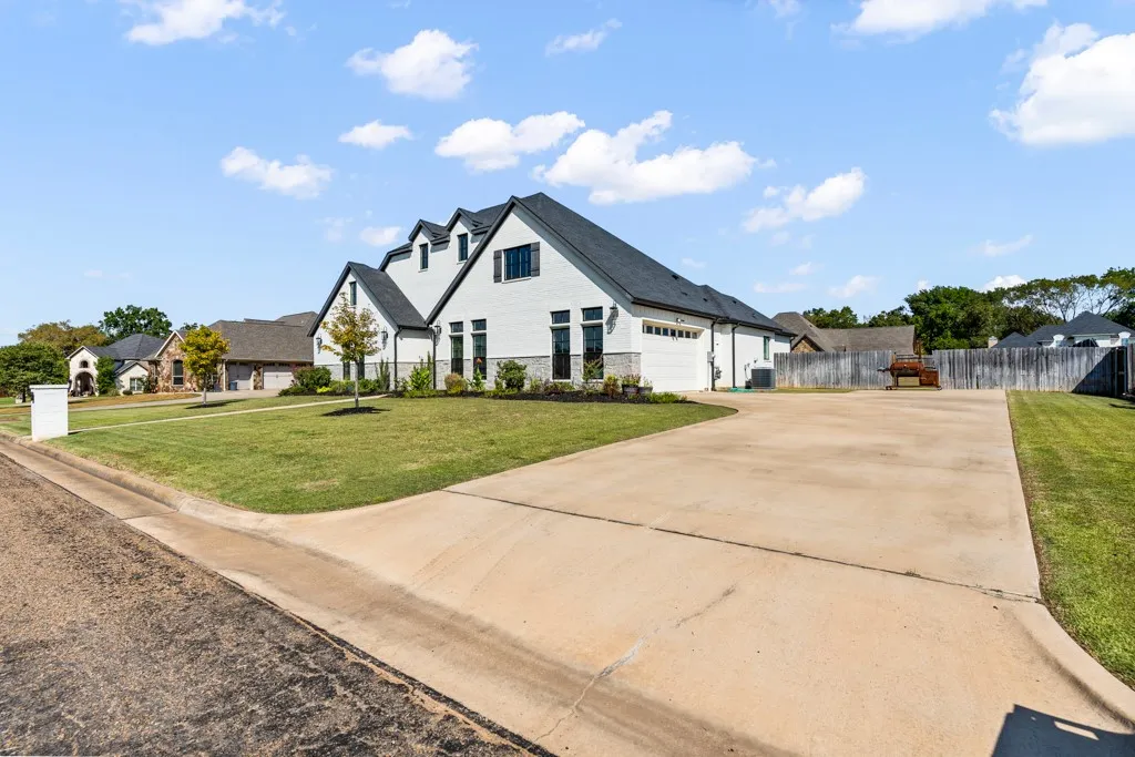 White brick exterior with a dark roof, multiple dormer windows, a concrete driveway, and a manicured lawn