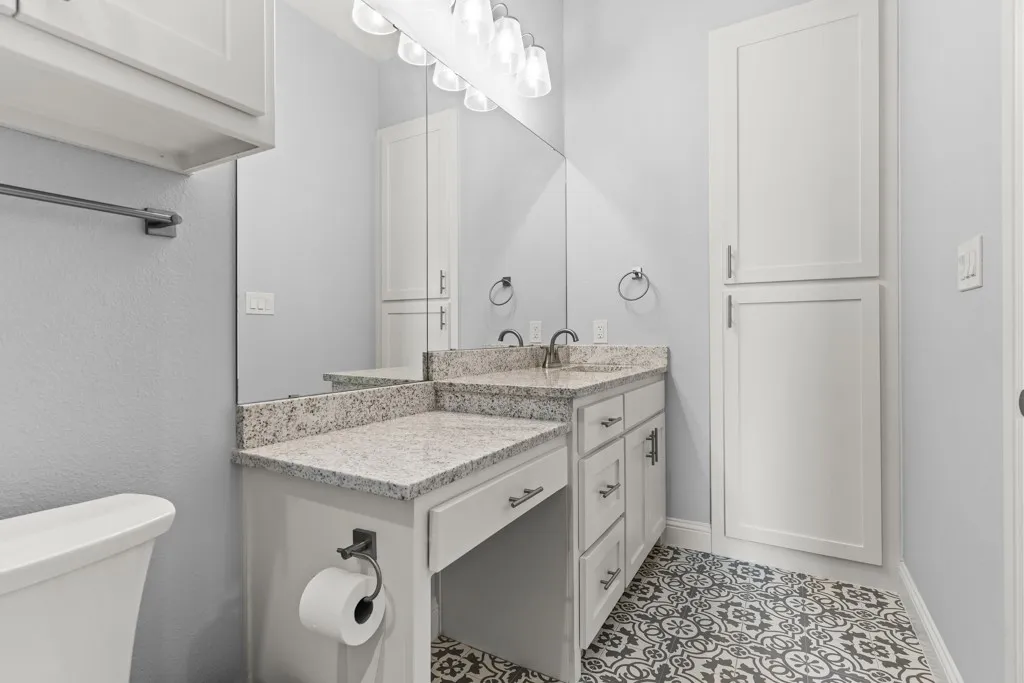 Dual vanity with granite-style countertops, custom cabinetry, large mirror, and patterned floor tile