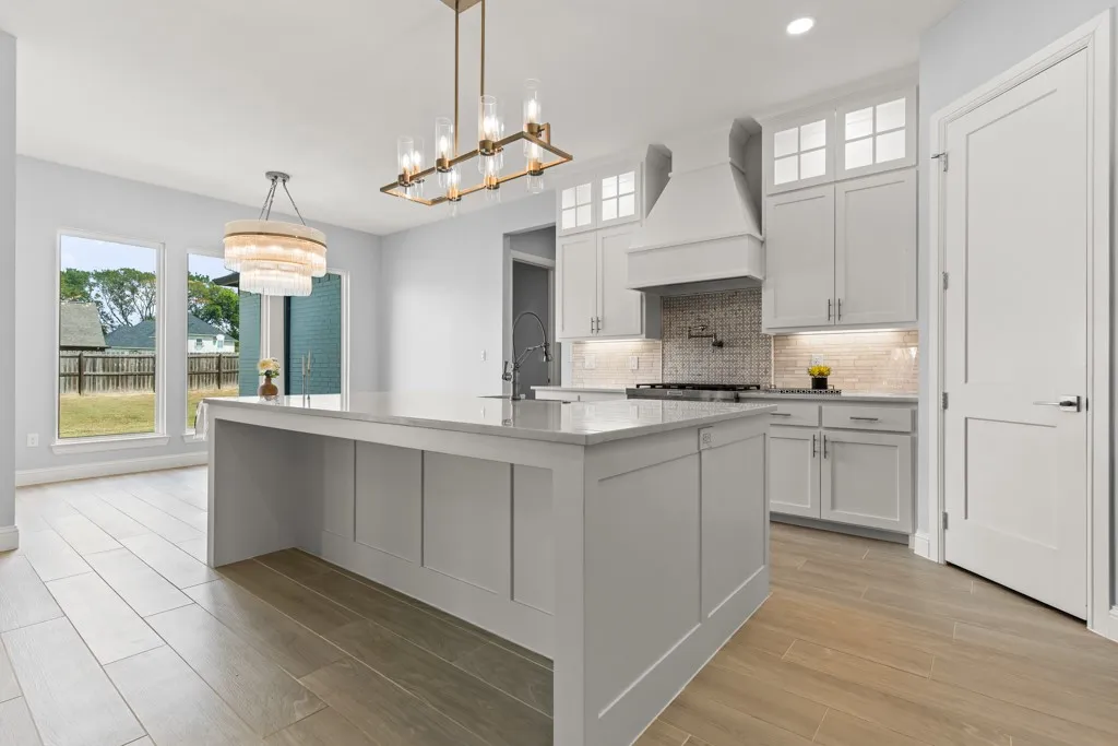 Spacious kitchen featuring a large central island, light cabinetry with upper glass-front accents, and wood-finish flooring