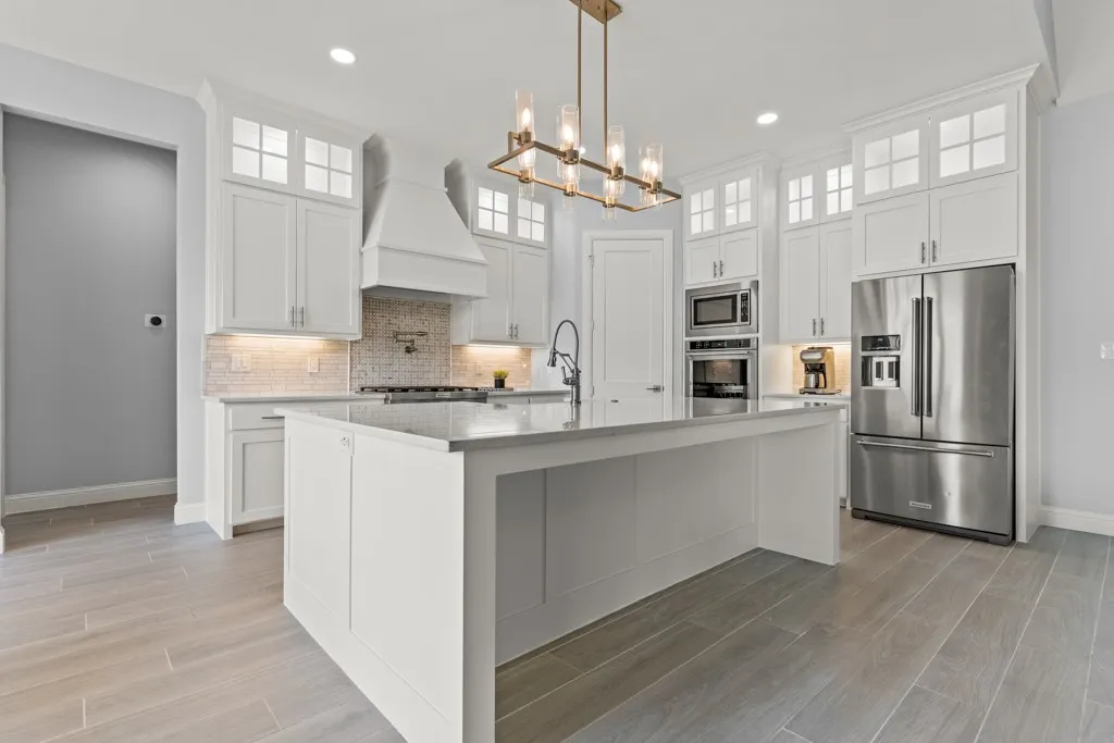 Kitchen with an expansive island featuring a solid surface countertop, white shaker cabinetry, stainless steel appliances, and wood-finish flooring