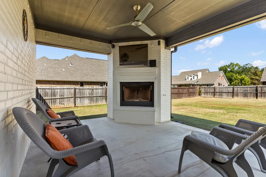 Covered patio featuring a ceiling fan, brick-clad fireplace, and concrete flooring