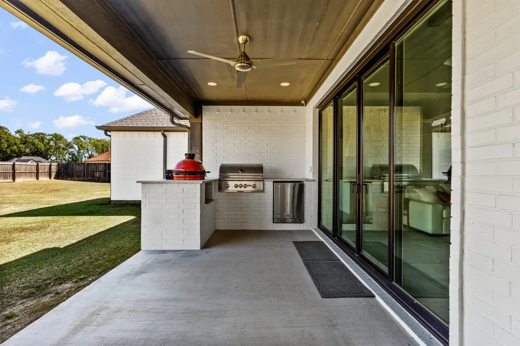 Covered patio featuring an outdoor kitchen with built-in grill, integrated beverage cooler, and white brick surround